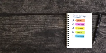 Notebook with text saying Goal Setting and S (specific) M (measurable) A (Attainable) R (reliable) T (time-bound)