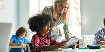 Teacher bending over to look at a document with a student