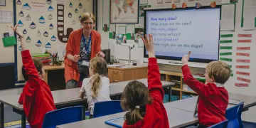 Teacher in front of class of students with their hands raised