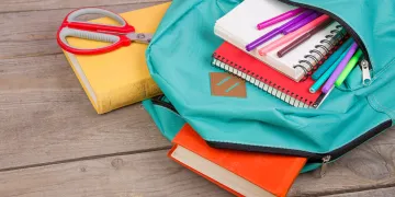Teal backpack with books, pens, notebooks and other school supplies coming from the pockets