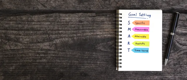 Notebook with text saying Goal Setting and S (specific) M (measurable) A (Attainable) R (reliable) T (time-bound)