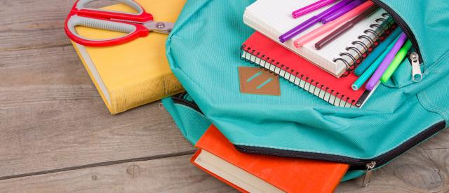 Teal backpack with books, pens, notebooks and other school supplies coming from the pockets