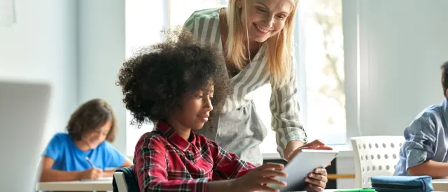 Teacher bending over to look at a document with a student