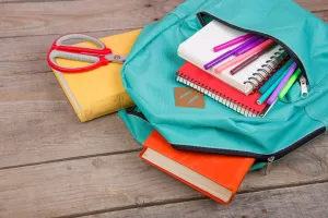 Teal backpack with books, pens, notebooks and other school supplies coming from the pockets